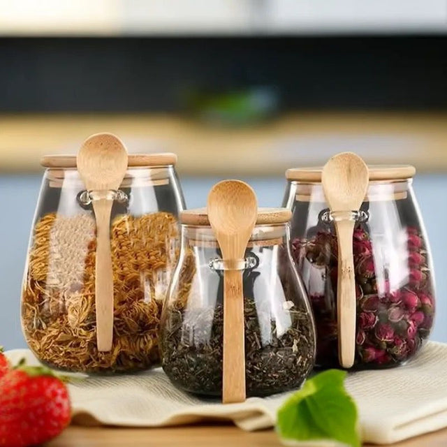 A set of borosilicate glass storage containers with bamboo lids and spoons, filled with various kitchen items such as grains and beans.