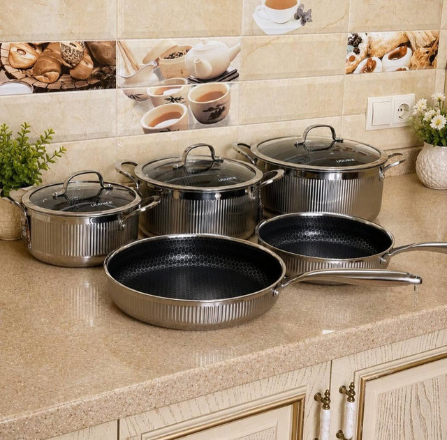 UCC LIFE 8-piece triply stainless steel cookware set with ribbed design, three casseroles with stainless steel lids, and two frying pans displayed on a modern kitchen countertop.