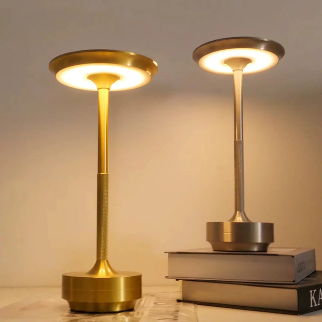 Two wireless table lamps with a gold finish, one larger than the other, illuminated and placed on a surface possibly indicating a touch control feature.