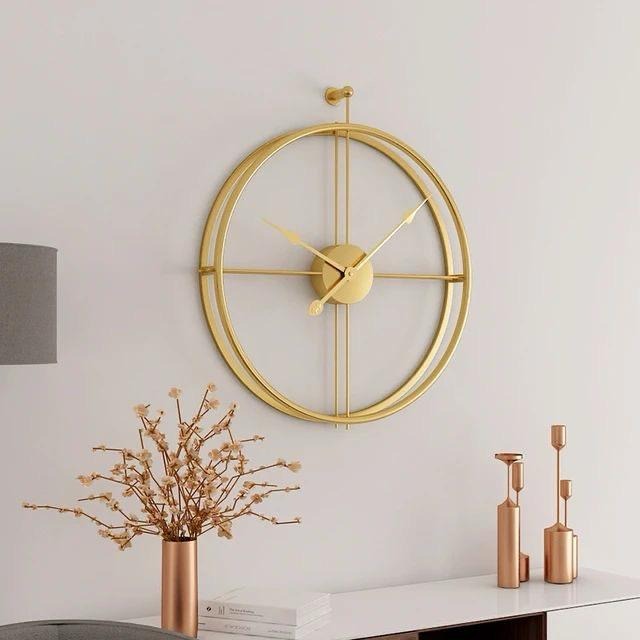 A large gold wall clock with a simple circular design, featuring a metallic frame and hands, mounted on a white wall above a decorative object and a candle holder.