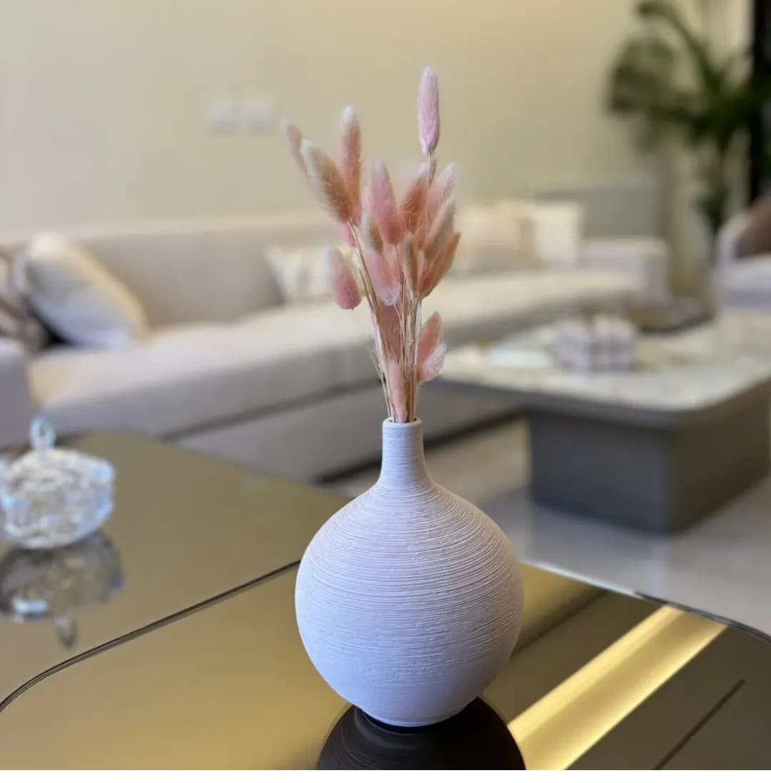White textured vase with dried pink flowers on a coffee table in a living room.