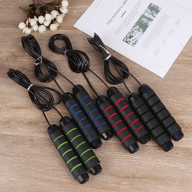 A set of multi-colored skipping ropes with foam handles, arranged on a wooden floor next to a book and a flower, for varied intensity workouts.
