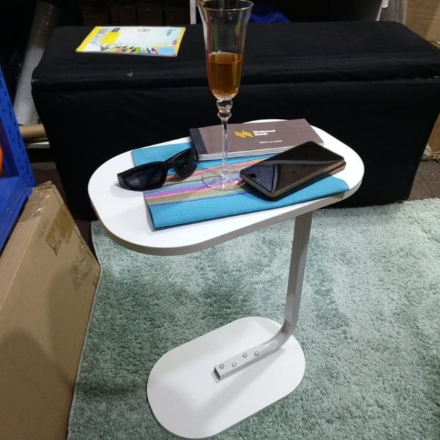 A white C-shaped side table with a glass of champagne and a mobile phone on top, placed on a green carpeted floor.