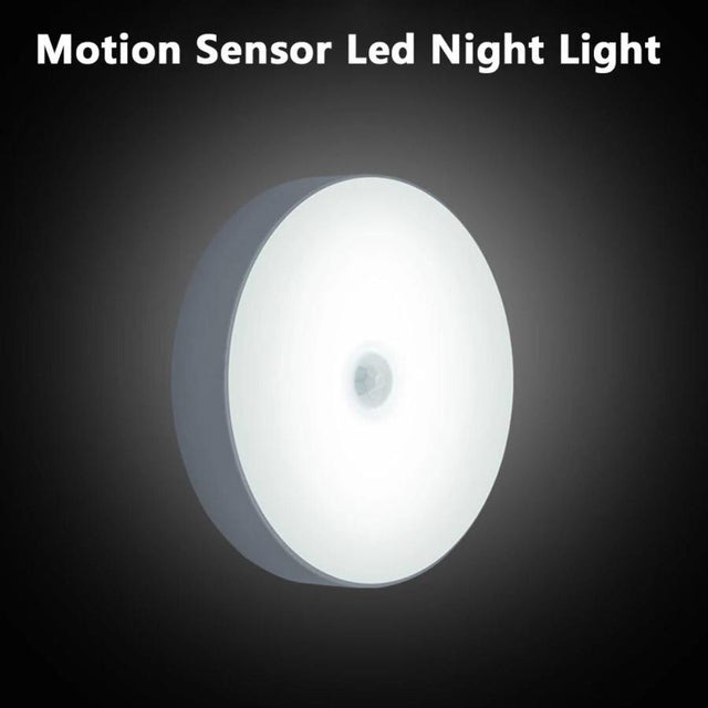 A motion sensor LED night light with a magnetic sticker, in a white circular design, illuminated in the dark.