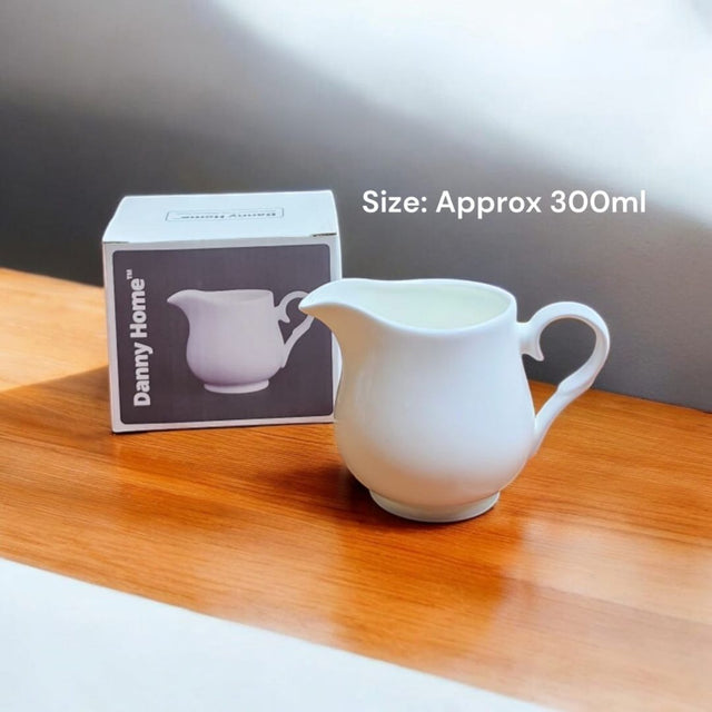 White ceramic pitcher on a wooden surface with a box labeled 'Darnly Home' in the background.