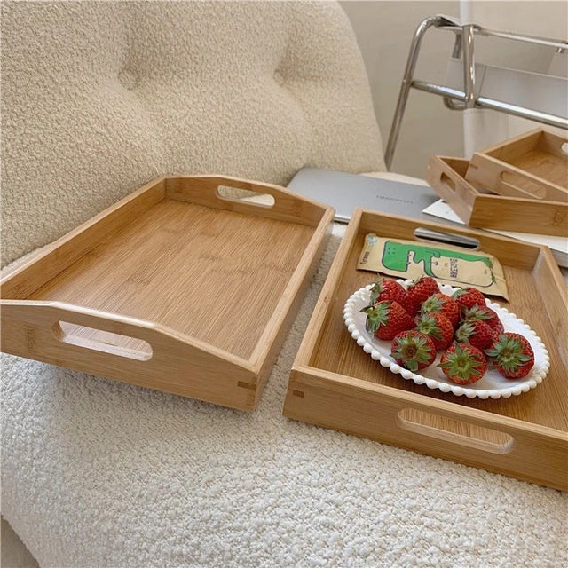 bamboo serving trays with handles, one empty and one carrying a plate of strawberries. The trays are placed on a white surface, possibly a sofa.