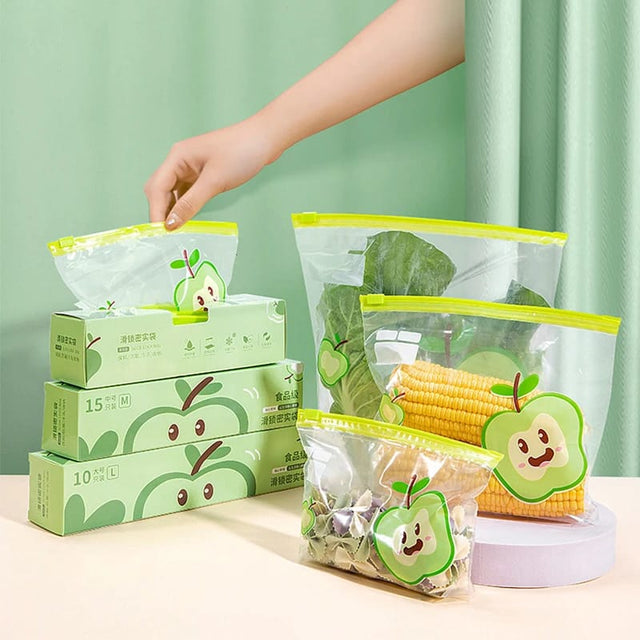 A set of reusable food storage bags in various sizes with a green and white design, featuring a plastic ziplock closure. Contents shown include apples, corn, and leafy greens.