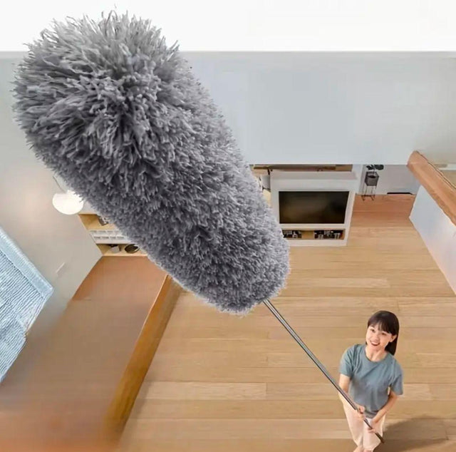 A person using a microfiber duster with an extendable handle to clean a high ceiling corner in a house.