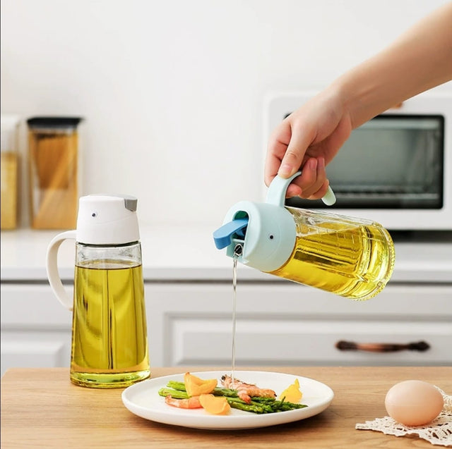 A person's hand pouring oil from a white and blue 630ml oil can dispenser onto a salad on a white plate, with a yellow bottle in the background.