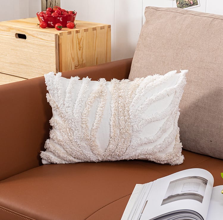 A beige and gray tufted coral cushion cover on a brown sofa with a magazine and a wooden side table in the background.