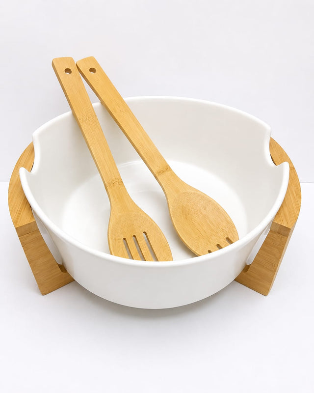 White ceramic salad bowl with bamboo stand and bamboo serving utensils filled with fresh salad