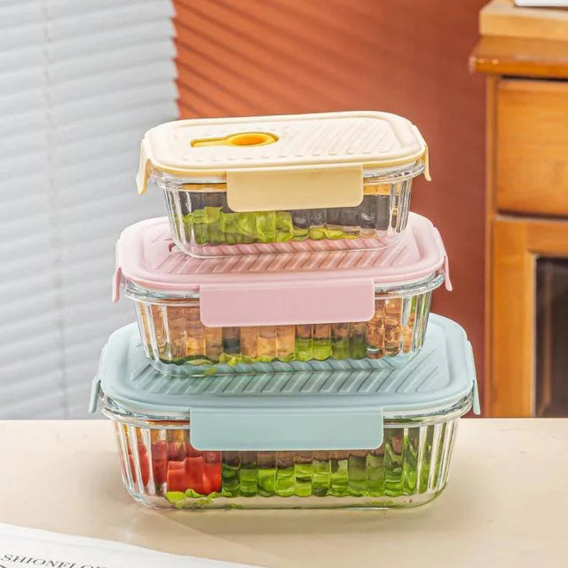 Set of three glass food containers with colorful lids on a kitchen counter.