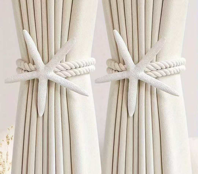 White starfish curtain tiebacks with twisted rope securing cream-colored curtains.