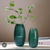 Textured green decorative vase set with artificial leafy branches displayed on a modern table.