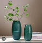 Textured green decorative vase set with artificial leafy branches displayed on a modern table.