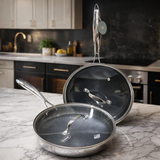 Two frying pans with glass lids on a marble countertop in a kitchen setting.