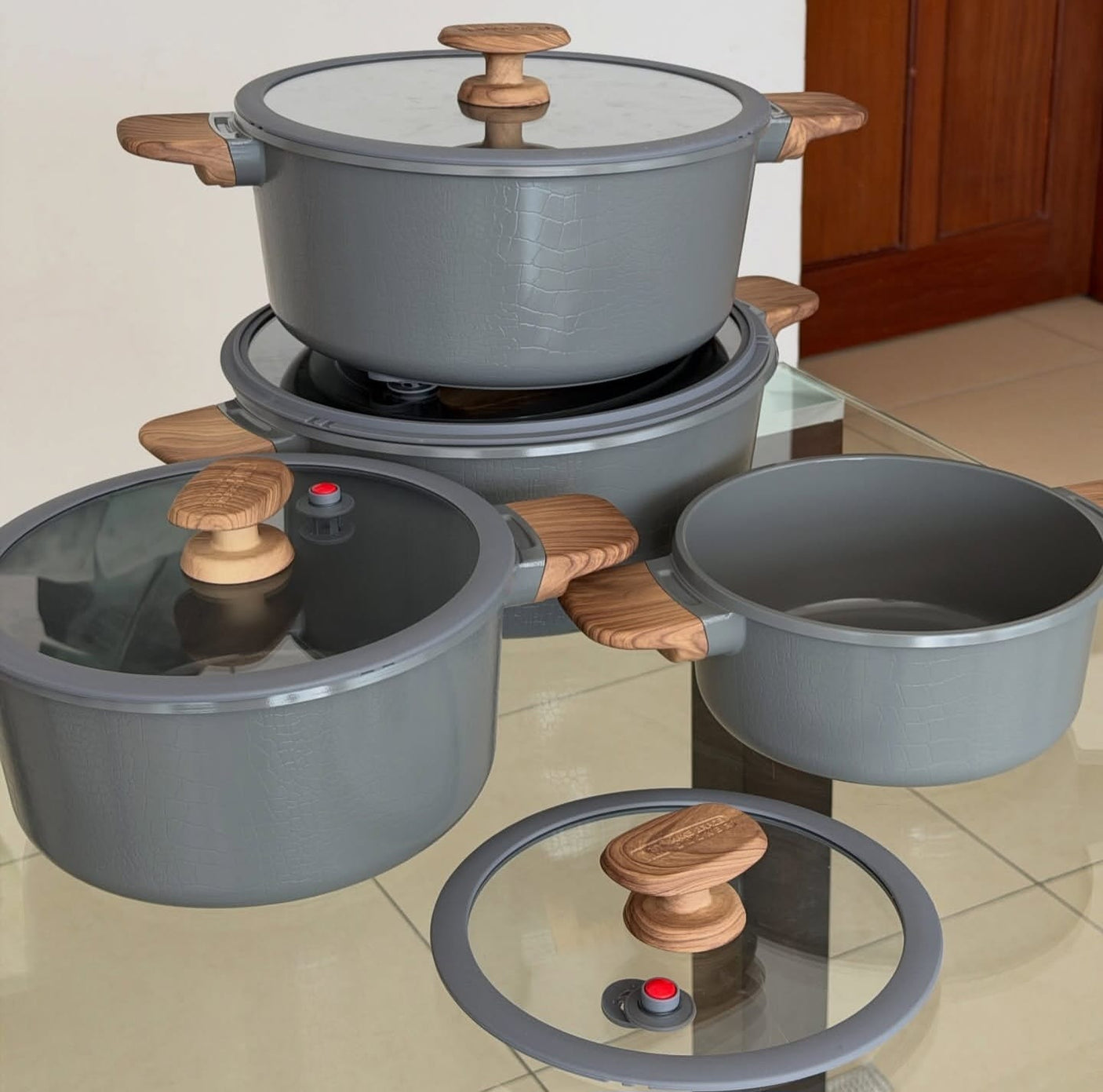 Set of gray cookware with wooden handles on a glass surface.