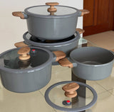 Set of gray cookware with wooden handles on a glass surface.