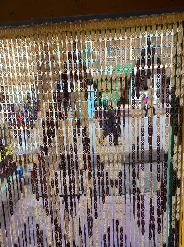 A plastic salon curtain with clear and opaque sections hanging on a rod, with people partially visible behind it.