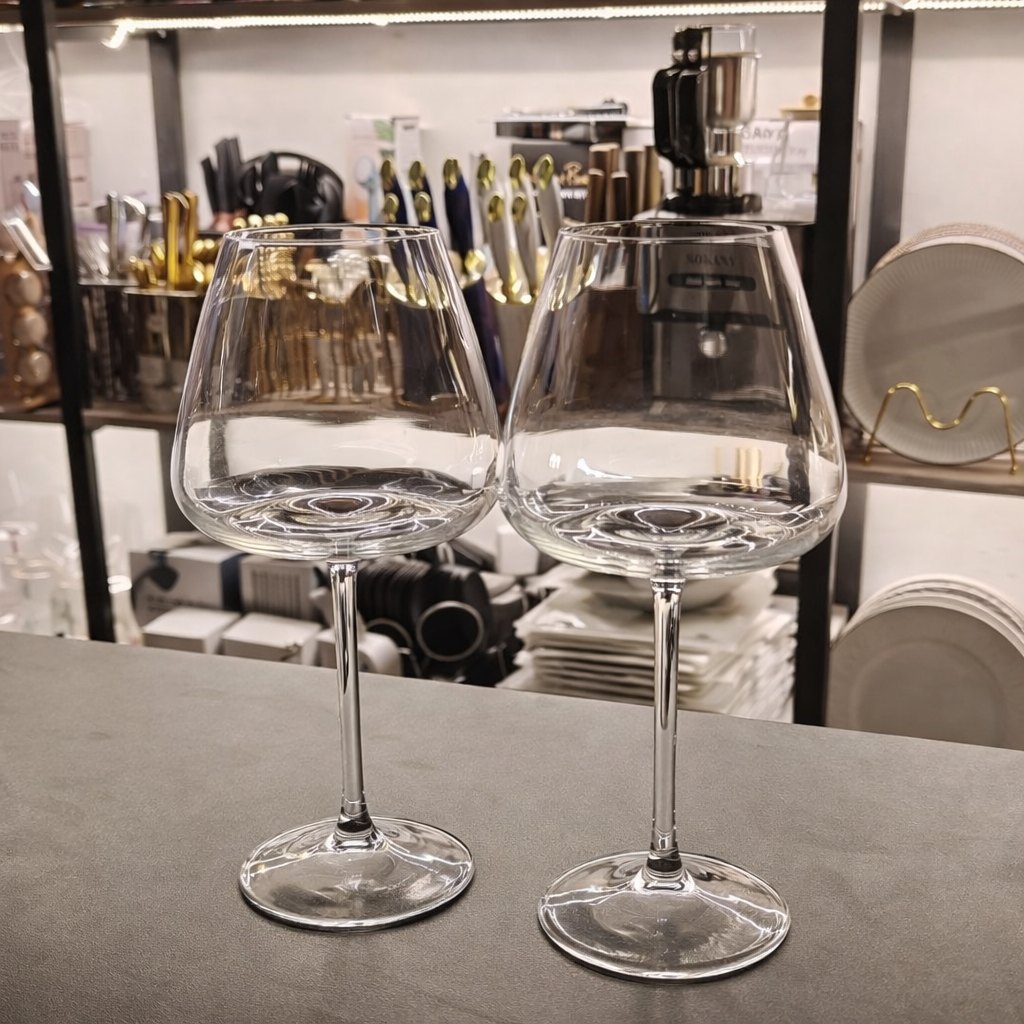 Two clear wine glasses on a table with a blurred background of kitchen items.