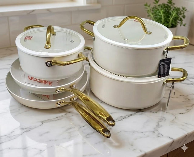 UCC Life 11-piece ceramic marble non-stick cookware set in matte black and cream white with gold handles, glass lids and silicone utensils on shelf