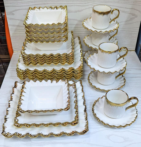 Material: Made from high-quality ceramic, offering strength and durability for everyday use and special occasions.

Design: Square-shaped plates and bowls with a sleek, modern finish that adds elegance to any dining setting.

Detailing: Each piece features a refined gold rim, giving a luxurious and classic appearance.

Set Includes: 6 dinner plates, 6 side plates, 6 soup bowls, 6 dessert bowls, and 6 mugs – ideal for a full table setting.

Color Scheme: Typically comes in white or ivory base to contrast bea