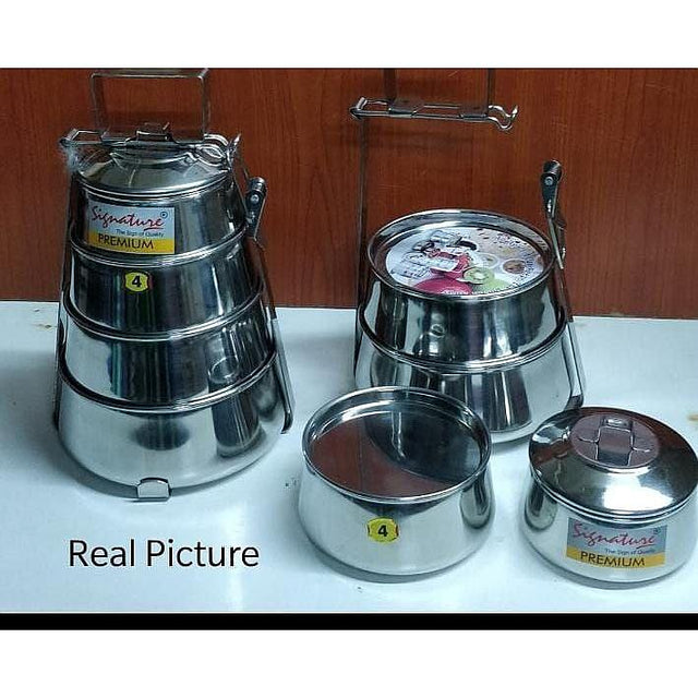 Set of stainless steel containers with lids on a white surface against a wooden background.
