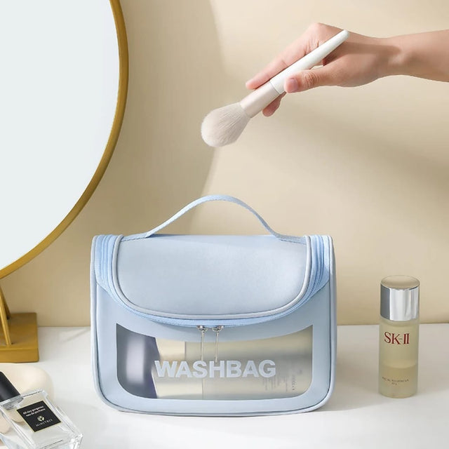 Clear travel washbag with SK-II product and makeup brush on a neutral background