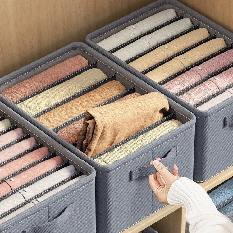 A set of gray fabric wardrobe organizers with dividers, displayed in a closet with various clothes neatly organized inside them.
