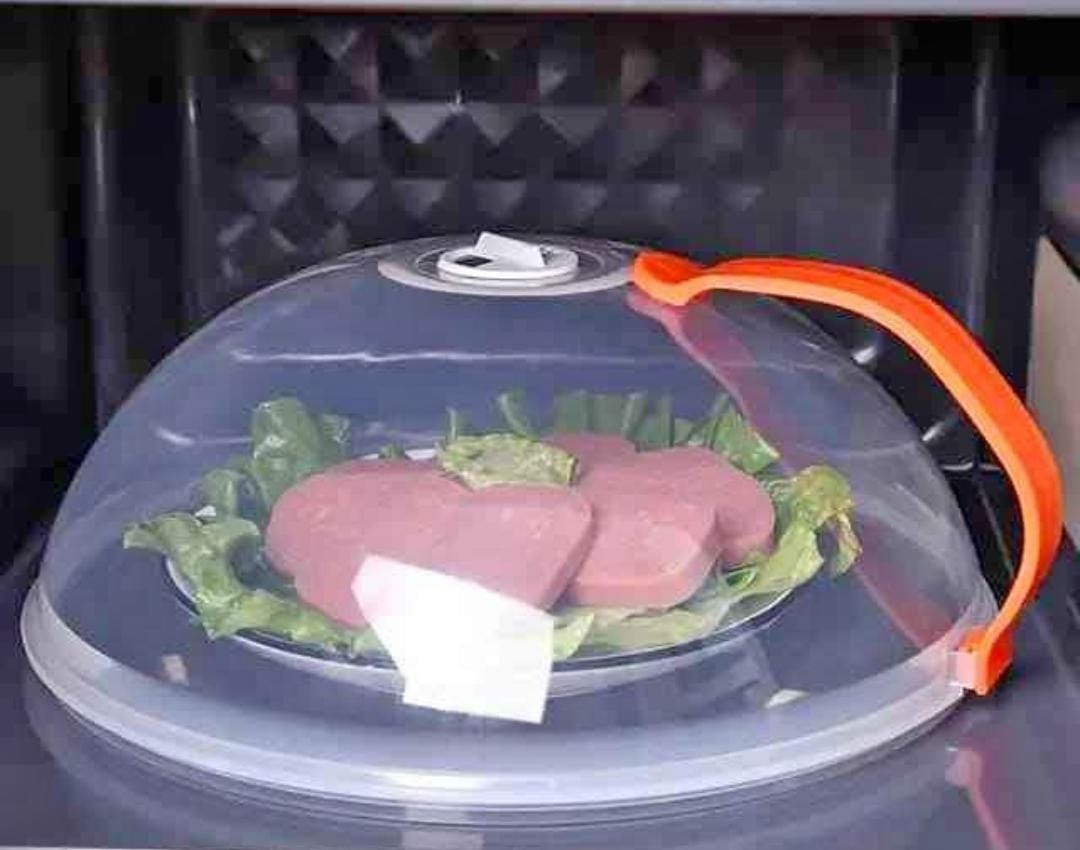 A clear microwave food cover with a orange handle, placed on top of a dish inside a microwave.
