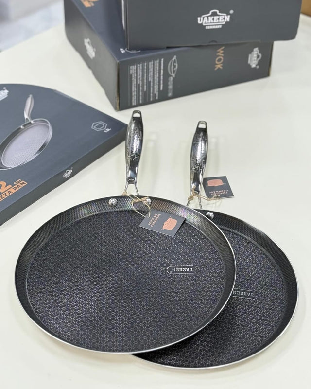 Two black frying pans with a textured surface on a white background, accompanied by their packaging.