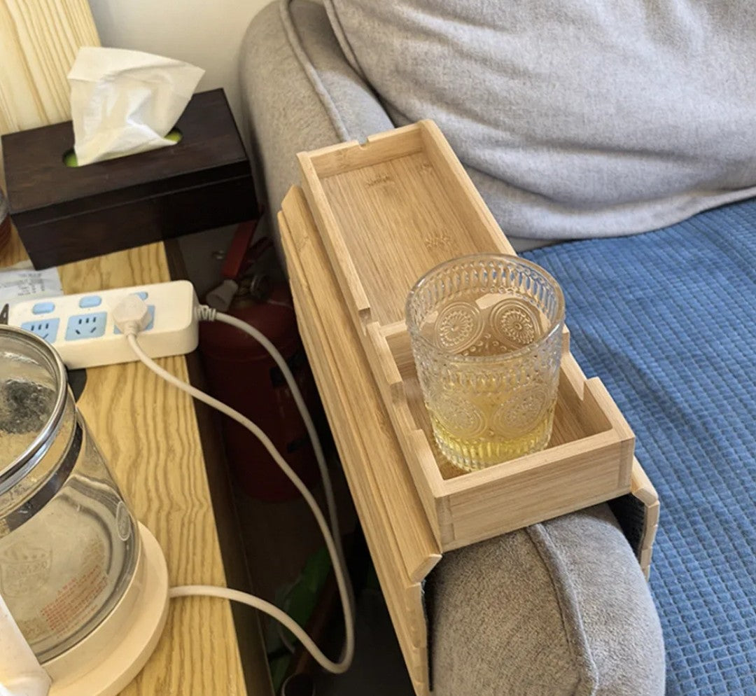 
Foldable natural bamboo sofa armrest tray measuring 16.3 by 13.3 inches with 5.1-inch built-in cup holder box, phone slot and flat surface for remote and snacks, shown clipped over a grey couch arm with a mug and TV remote — available at iDecorators Kenya, Nairobi.
