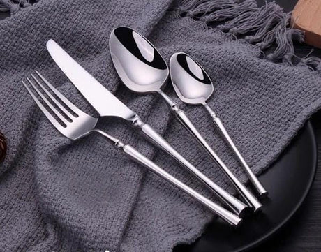 Set of silver cutlery including a fork, knife, and two spoons on a textured gray surface.