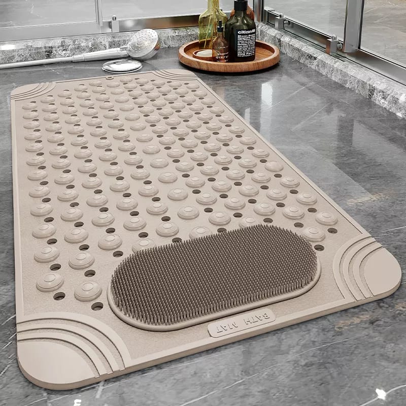 An anti-slip beige bathroom mat with a textured surface, placed on a tiled floor. The mat appears to be rectangular with raised edges and a brush-like texture on one section, indicating a non-slip surface.