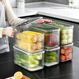 A set of three clear acrylic fridge organizers with lids, containing various fruits and vegetables, placed on a kitchen countertop.