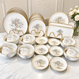 30-piece white porcelain dinner set with gold tree design, including dinner plates, side plates, bowls, cups, saucers, and serving platters displayed on a marble table.