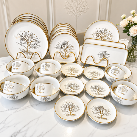 30-piece white porcelain dinner set with gold tree design, including dinner plates, side plates, bowls, cups, saucers, and serving platters displayed on a marble table.