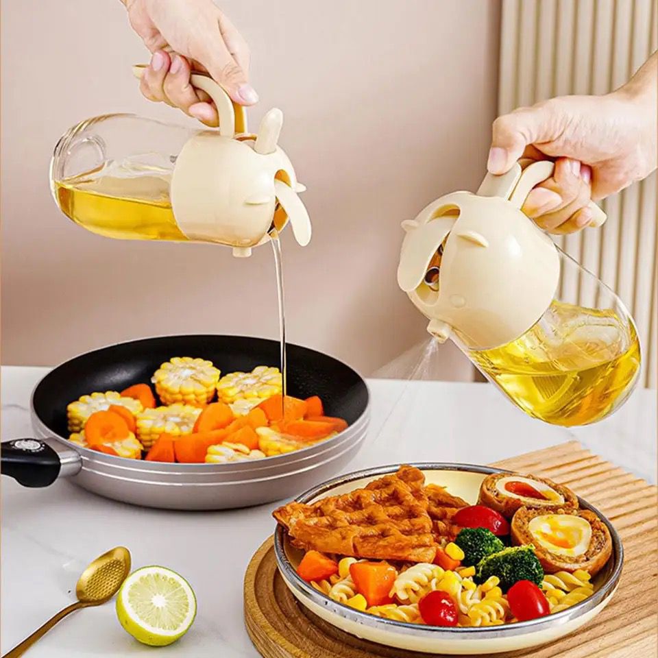 A person is shown using a glass oil spray bottle with a pour spout nozzle. The bottle is being tilted to dispense oil over food in a pan, demonstrating the dual functionality of the product.