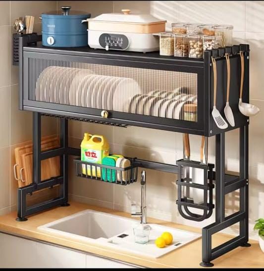 Black steel over-sink kitchen rack with dust-proof dish cabinet, top shelf for appliances, side utensil hooks, and mid-level wire basket mounted above a kitchen sink