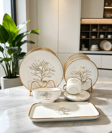 30-piece white porcelain dinner set with gold tree design, including dinner plates, side plates, bowls, cups, saucers, and serving platters displayed on a marble table.