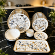 30-piece marble pattern porcelain dinner set with gold rims, featuring dinner plates, side plates, soup bowls, cups, saucers, and serving platter on a black marble countertop.