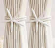 White starfish curtain tiebacks with twisted rope securing cream-colored curtains.