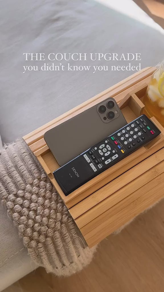 
Foldable natural bamboo sofa armrest tray measuring 16.3 by 13.3 inches with 5.1-inch built-in cup holder box, phone slot and flat surface for remote and snacks, shown clipped over a grey couch arm with a mug and TV remote — available at iDecorators Kenya, Nairobi.