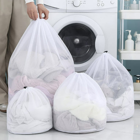 Reusable white mesh laundry wash bags in four sizes placed in front of a washing machine, filled with clothes.