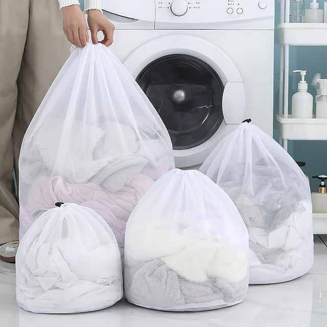 Reusable white mesh laundry wash bags in four sizes placed in front of a washing machine, filled with clothes.